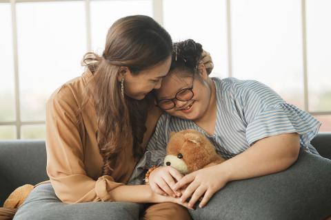 Caregiver hugging child. Child is holding a stuffed animal.